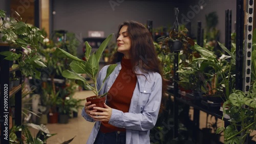 Indoor urban plant shop scene with cheerful woman examining potted greenery carefully