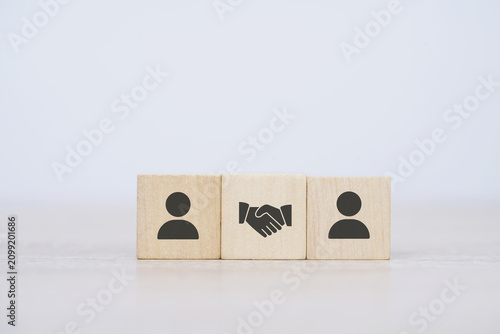 wood cube block with handshake agreement icon symbol between two person cubes, concept of business, deal, partnership or cooperation between parties and sales according to business goals.