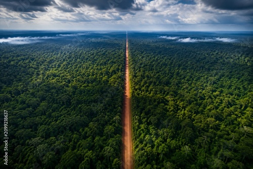 Aerial view of a dirt road cutting through a dense tropical rainforest.