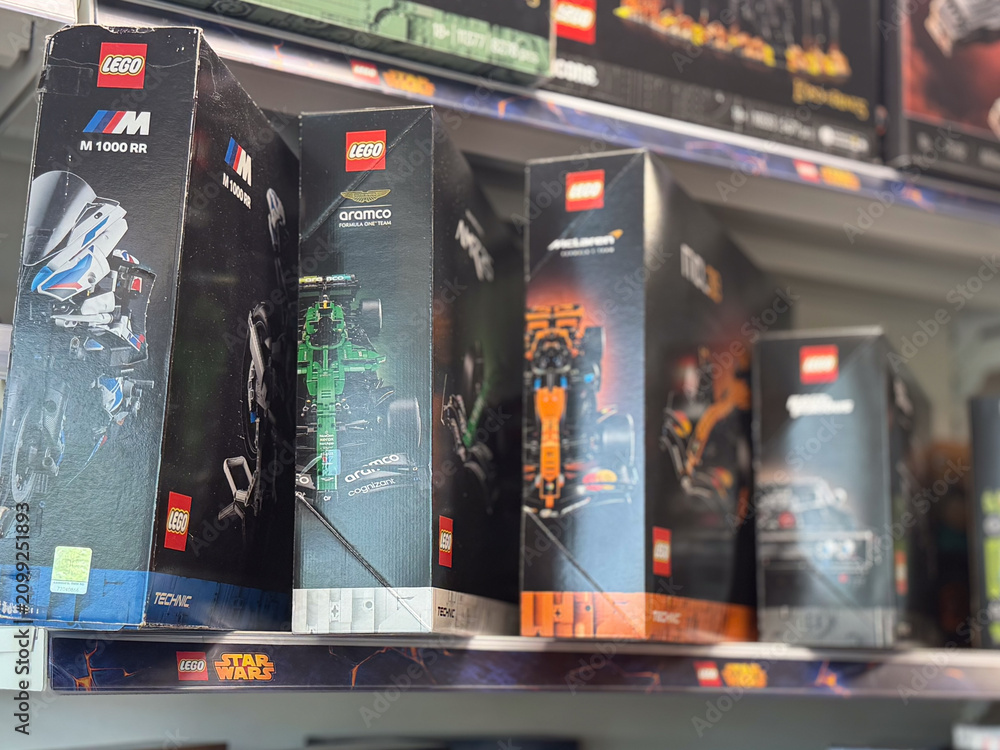 Fototapeta premium Rows of lego model boxes displayed on a store shelf in a toy aisle, with racing and space sets visible in a blurred retail background.