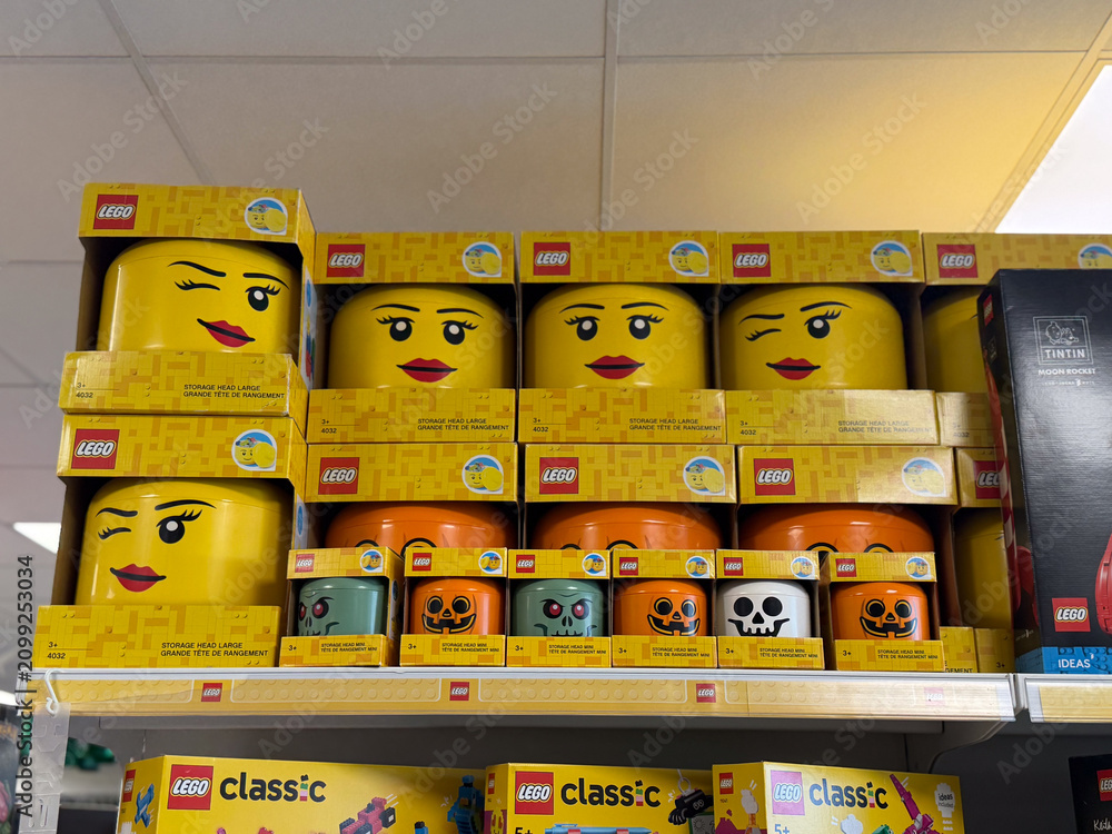 Fototapeta premium Toy store shelf with stacked lego boxes and halloween-themed storage heads in bright yellow colors on a retail display