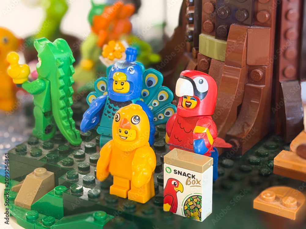 Obraz premium Colorful toy animals and bird figures in a jungle play scene with a snack box, showing a playful and creative building set on a green base.