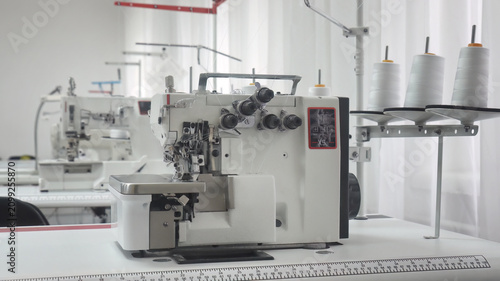 Bild auf Leinwand Industrial overlock sewing machine with white thread spools in workshop
