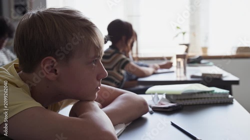 Caucasian teenage boy resting head on desk in classroom, waking up and looking tiredly towards front. Clip for educational campaigns on student fatigue