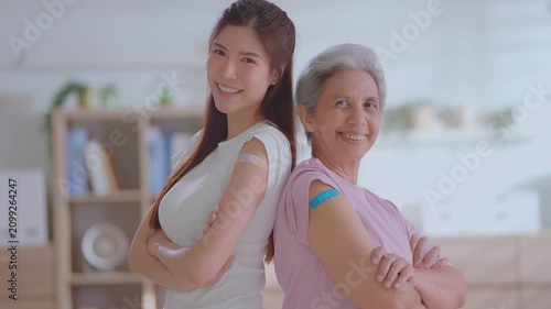 Senior mother and adult daughter showing adhesive bandages on their arms after vaccination. Concept for covid-19 vaccine, flu shot, elderly health protection, family care, and immune booster.
