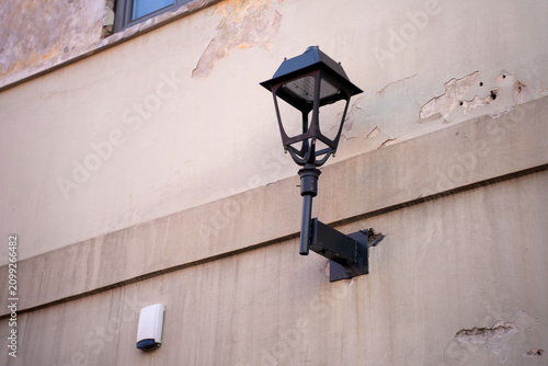 Bild auf Leinwand black metal lantern on a mounting bracket affixed to a weathered beige stucco bu