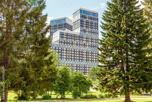 Modern high-rise residential complex Clever Park surrounded by tall coniferous trees and green lawns, urban living with nature integration, contemporary architecture in a landscaped environment
