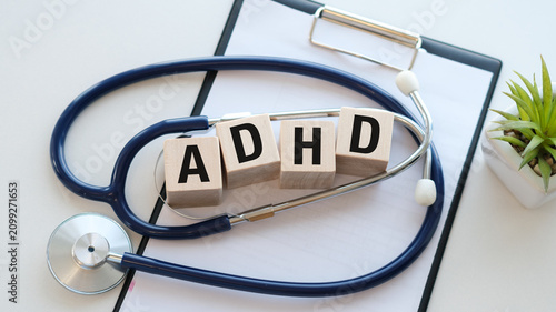 Conceptual medical photography featuring wooden blocks with the letters ADHD inside a blue stethoscope on a white surface, representing diagnosis, attention deficit 