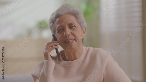 Older asian woman using mobile phone sitting relaxed on couch at home, smile or laugh with happy time. enjoy watch or read text on social media app. Senior asian with digital technology after retired.