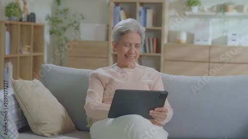 Older asian woman using tablet sitting relaxed on couch at home, smile or laugh with happy time. enjoy watch or read text on social media app. Senior asian with digital technology after retired.