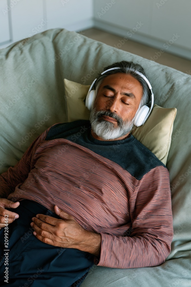 Fototapeta premium Middle aged man reclining with headphones on couch for relaxation background and wellness banner design