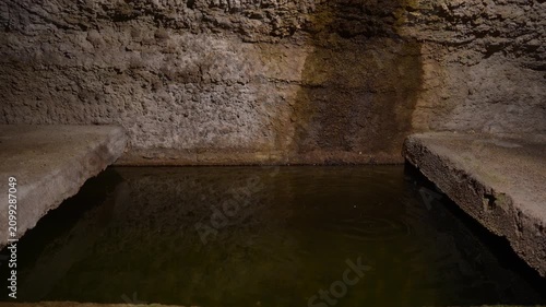 A water drop falls in slow motion into an old medieval stone cistern