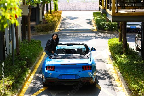 A stylish Asian girl stands on a blue convertible.