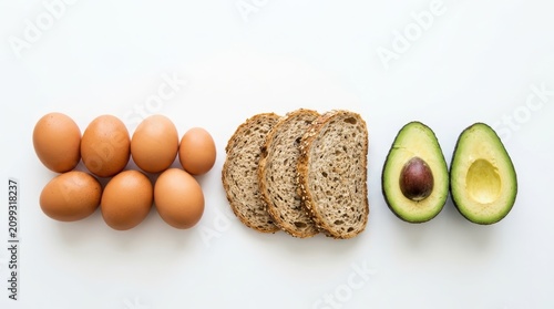 Breakfast ingredients including eggs, bread and avocado on a white background