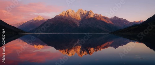 Majestic mountain range reflects in still lake during colorful sunrise or sunset golden hour
