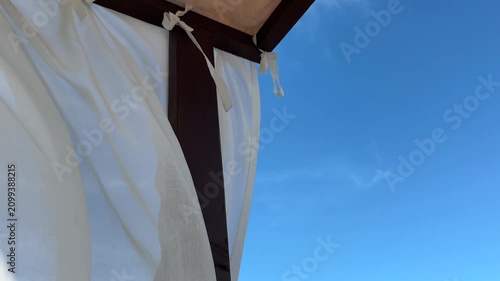 White curtains on wooden outdoor cabana against clear blue sky, quiet luxury resort design, wellness retreat, slow travel and peaceful summer hospitality concept.