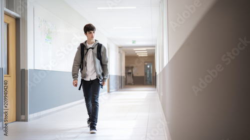 Student in Hallway: A young student with a backpack walks down a bright school hallway, conveying a sense of journey and everyday life.