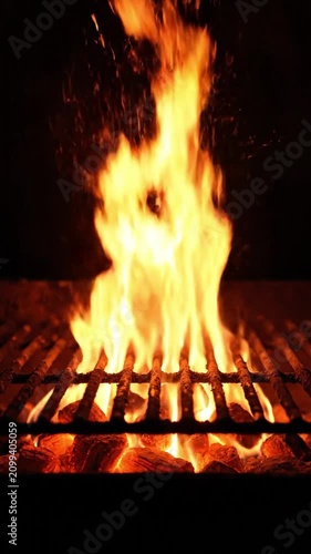 Intense flames erupting on a barbecue grill with glowing charcoal and sparks on black background