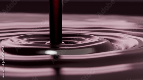 Dropping thin stream striking glossy deep maroon pool on table forming mound and rippling outward