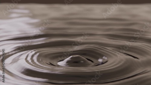 Falling primary droplet striking sepia pool in shallow tray, creating crown and ringed ripples