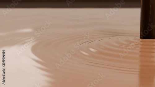 Touching vertical rod causing ripples on brown liquid in shallow tray on tabletop, observing decay