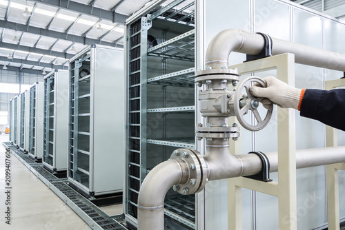 Foto Industrial facility with server racks and a worker adjusting a valve