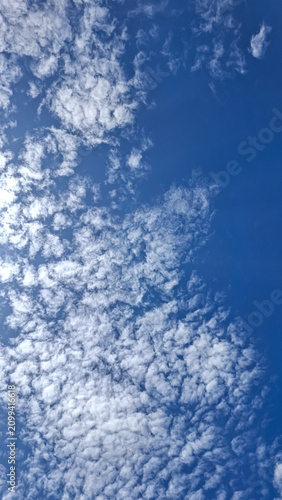 Bild auf Leinwand Vertical view of fluffy white clouds on a bright blue sky