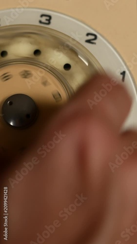 Close-up of a finger dialing a telephone number on a vintage rotary dial phone in vertical video