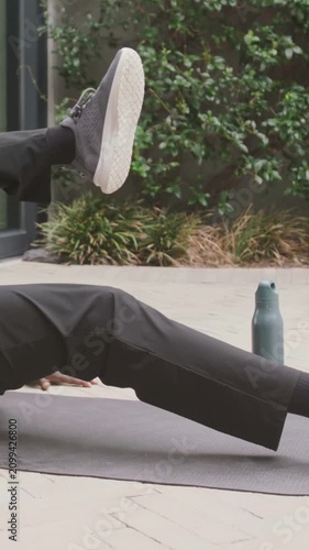 Vertical video: Lying man in dark pants starting alternate leg lifts on patio for core near bottle
