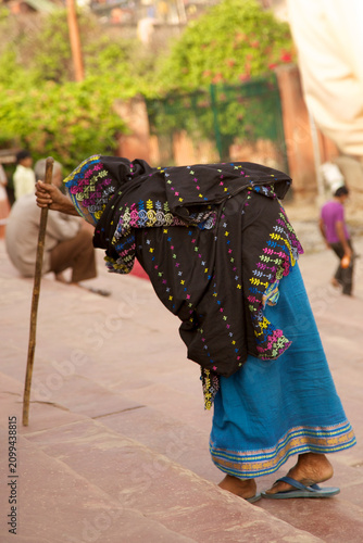 Foto An elderly woman wearing a traditional black and blue sari slowly ascends stone steps with the aid of a wooden walking stick
