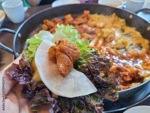 Hand Holding Korean Style Lettuce Wrap Ssam with Spicy Stir Fried Chicken and Pickled Radish