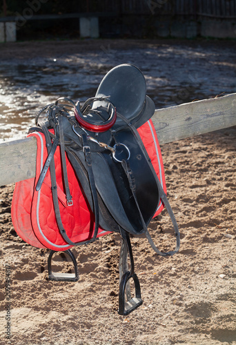 horse saddle hangs on wooden fence in farmyard