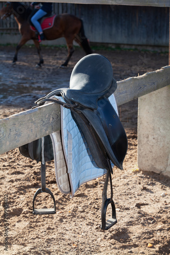 horse saddle hangs on wooden fence with horse in background