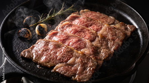 Premium Wagyu beef teppanyaki steak sliced on a dark grill pan. Sizzling marbled meat with garlic and herbs. Cinematic mood lighting for luxury Japanese dining menus look.