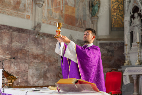 Canvas Print The priest holds the chalice high during a Holy Mass in a historic church in Europe, conducting the Eucharistic celebration and prayer