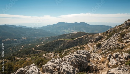 Winding Road Through Mountains in Daytime With Clear Blue Sky and Distant Hills