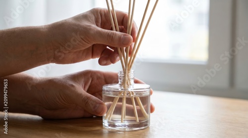Hands arranging natural wooden sticks inside a glass bottle of liquid reed diffuser for home fragrance