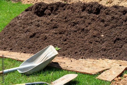 Obraz na plátně Large pile of dark, rich organic soil or compost ready for gardening and planting, with a shovel and trowel resting on wood, symbolizing outdoor yard work and soil preparation