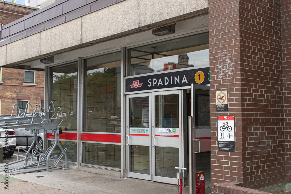 Obraz premium Toronto, ON, CANADA - Aug 8 2024 : Entrance to the TTC Spadina subway station in Toronto with a sign, a yellow Line 1 marker, glass doors with a red stripe, a bicycle repair stop notice.