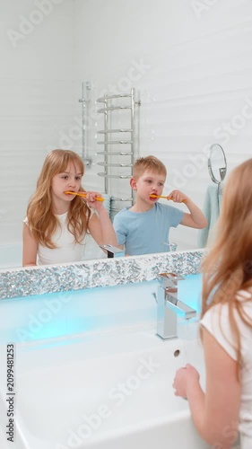 Boy and girl, brother and sister standing in bathroom in front of mirror carefully brushing their teeth. Children kids focused on daily hygiene routine promoting dental health and personal care habits