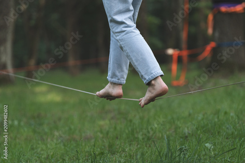 Bare feet gripping orange slackline between trees, finding balance and staying grounded in life wellness and mindfulness concept.