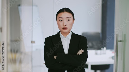 Focused Asian Woman In Business Suit, Standing With Crossed Arms In Office Setting, Exuding Confidence And Professionalism. Ideal Image For Business Concept And Corporate Environments.