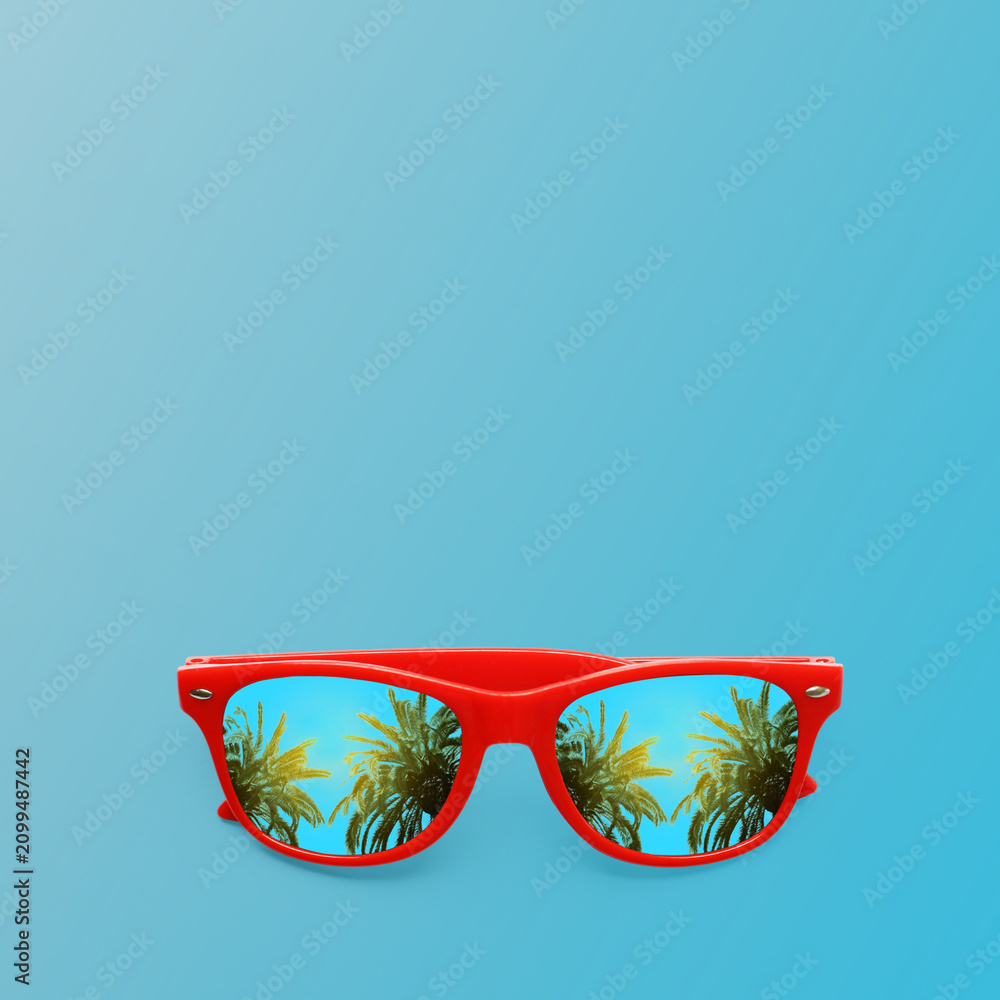 Obraz premium Stylish sunglasses on light blue background. Tropical palm trees on sunny day reflecting in lenses