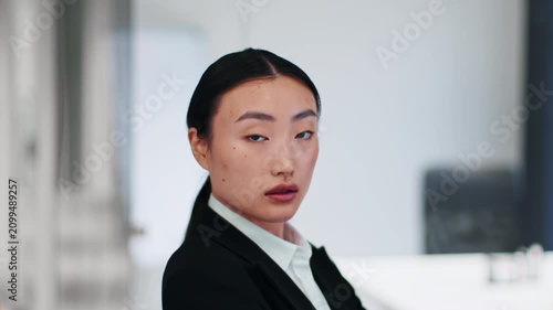 Focused Young Asian Woman With Professional Attire Looking Over Shoulder In Modern Office Environment, Engaged In Work Or Business Activity, Conveying Confidence And Determination. Business Concept.