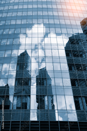 Tall glass skyscrapers of business offices in city reflect blue sky, clouds, and other skyscrapers. Sunlight glistens on glass surface. modern cityscape of  city's business district. vertical