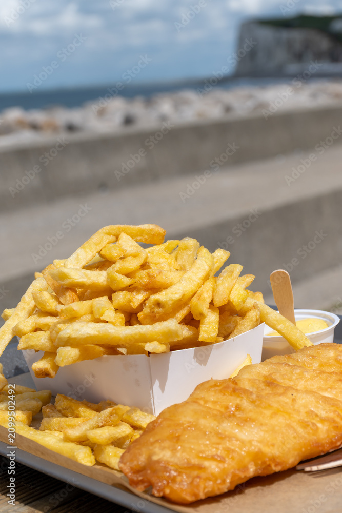 Fototapeta premium Fish and chips on Le Treport promenade — golden battered cod with mountain of french fries, seaside flavors enjoyed outdoors by the harbor in Normandy, France