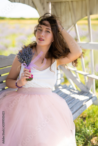 a beautiful girl in a dress with a bouquet of lavender flowers sits on a bench