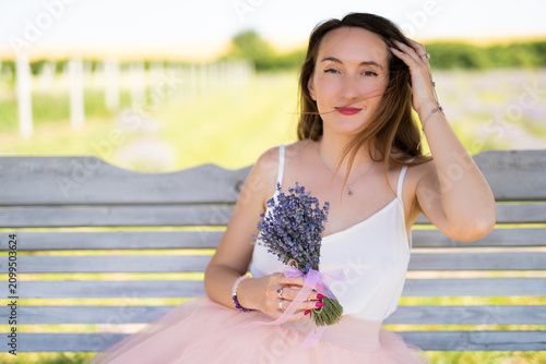 a beautiful girl in a dress with a bouquet of lavender flowers sits on a bench
