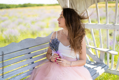 a beautiful girl in a dress with a bouquet of lavender flowers sits on a bench