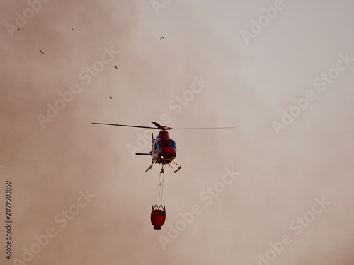 Aerial Firefighting Helicopter with Water Bucket in Smoky Sky